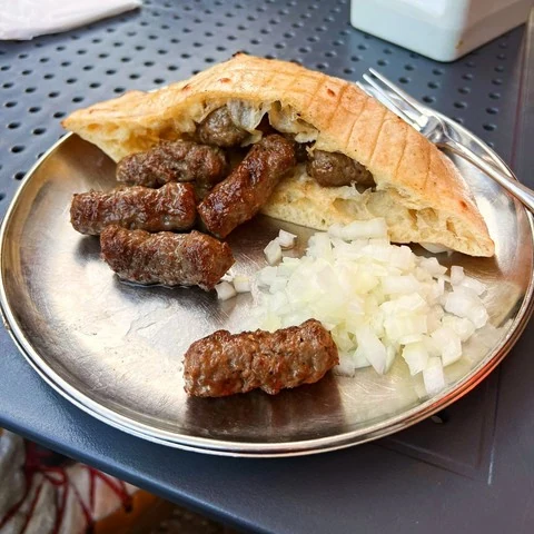 Grilled cevapi with flatbread and chopped onion on a metal tray